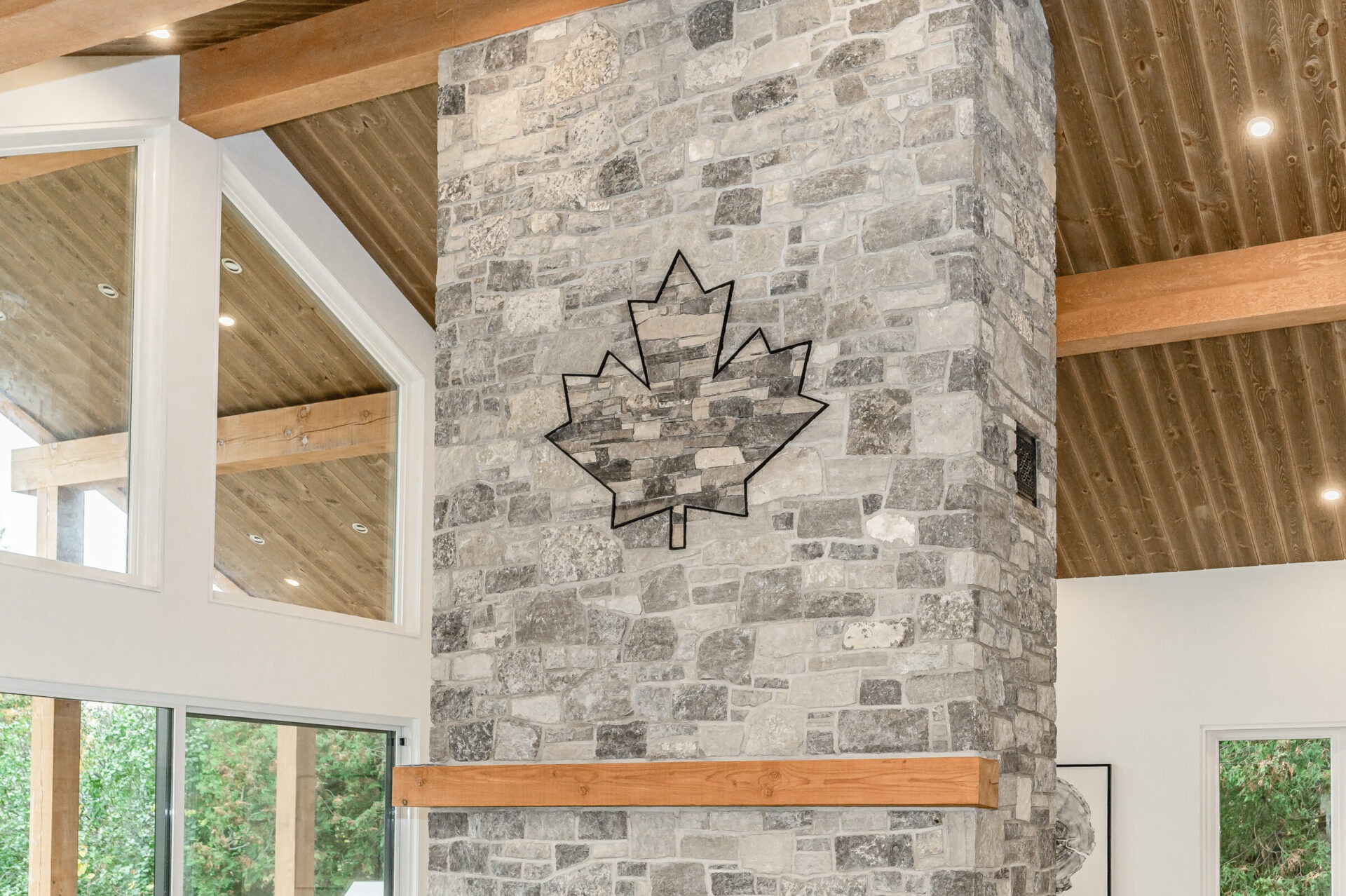 This interior features a stone pillar with a large maple leaf design, wooden beams, recessed lighting, and large windows in a modern setting.