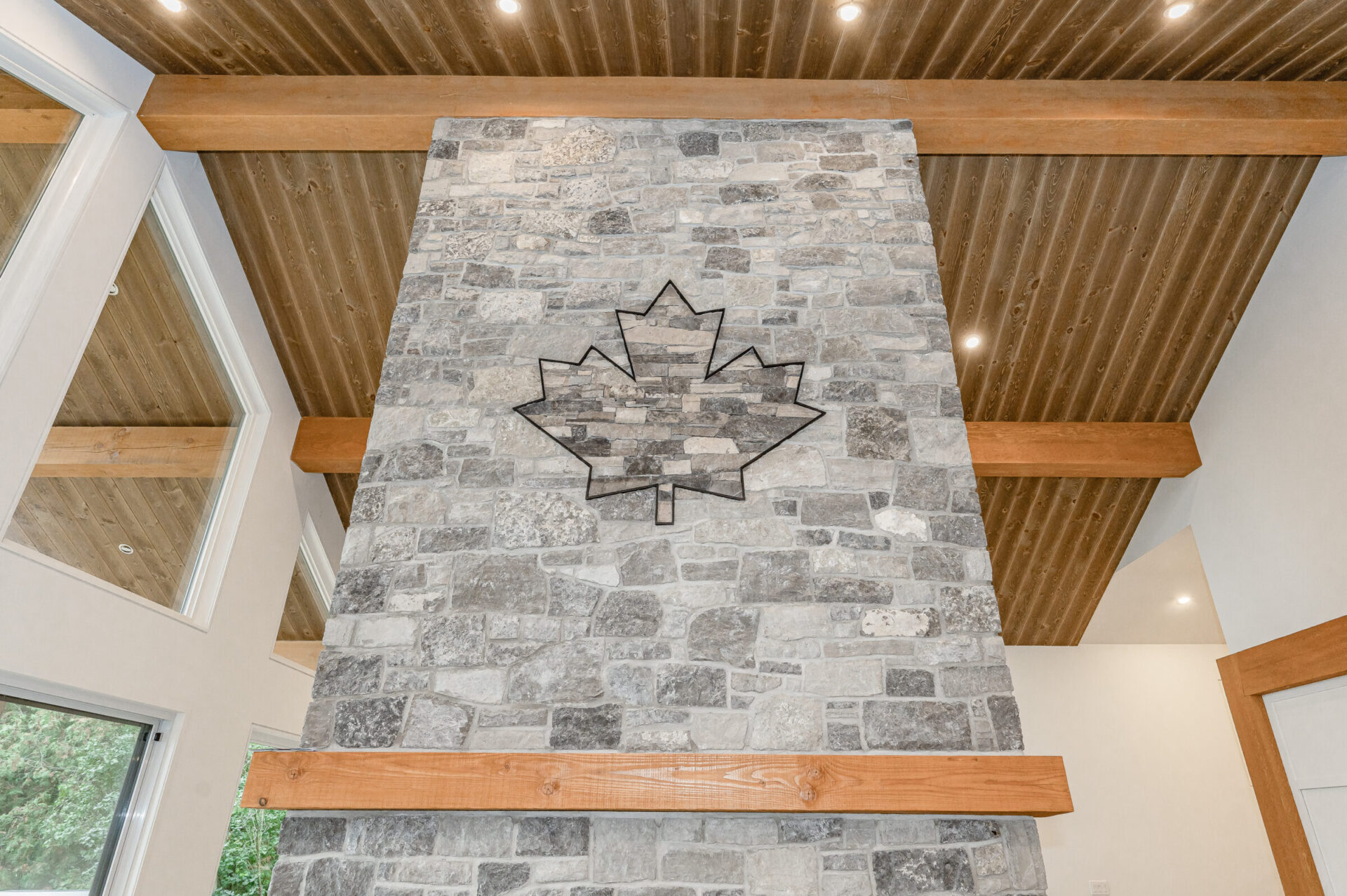 This image features an interior space with a stone wall with a leaf-shaped design inlay, wooden ceiling beams, recessed lighting, and door frames.