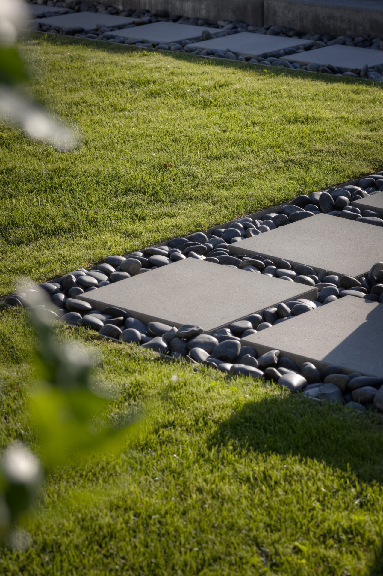 A landscaped garden featuring patterned stepping stones surrounded by smooth pebbles and lush green grass, implying a serene and meticulously designed outdoor space.