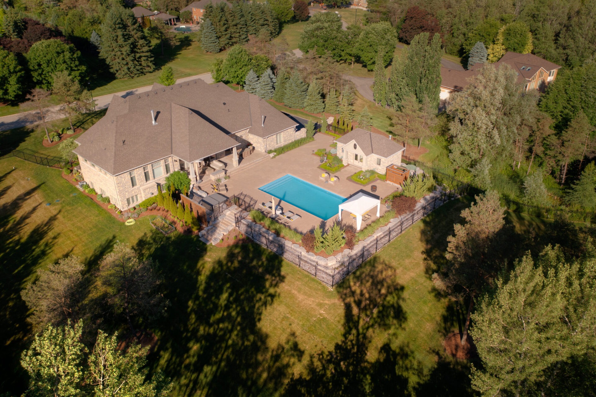 An aerial view of a large estate featuring a stone house with a swimming pool, landscaped gardens, and surrounded by lush greenery and trees.