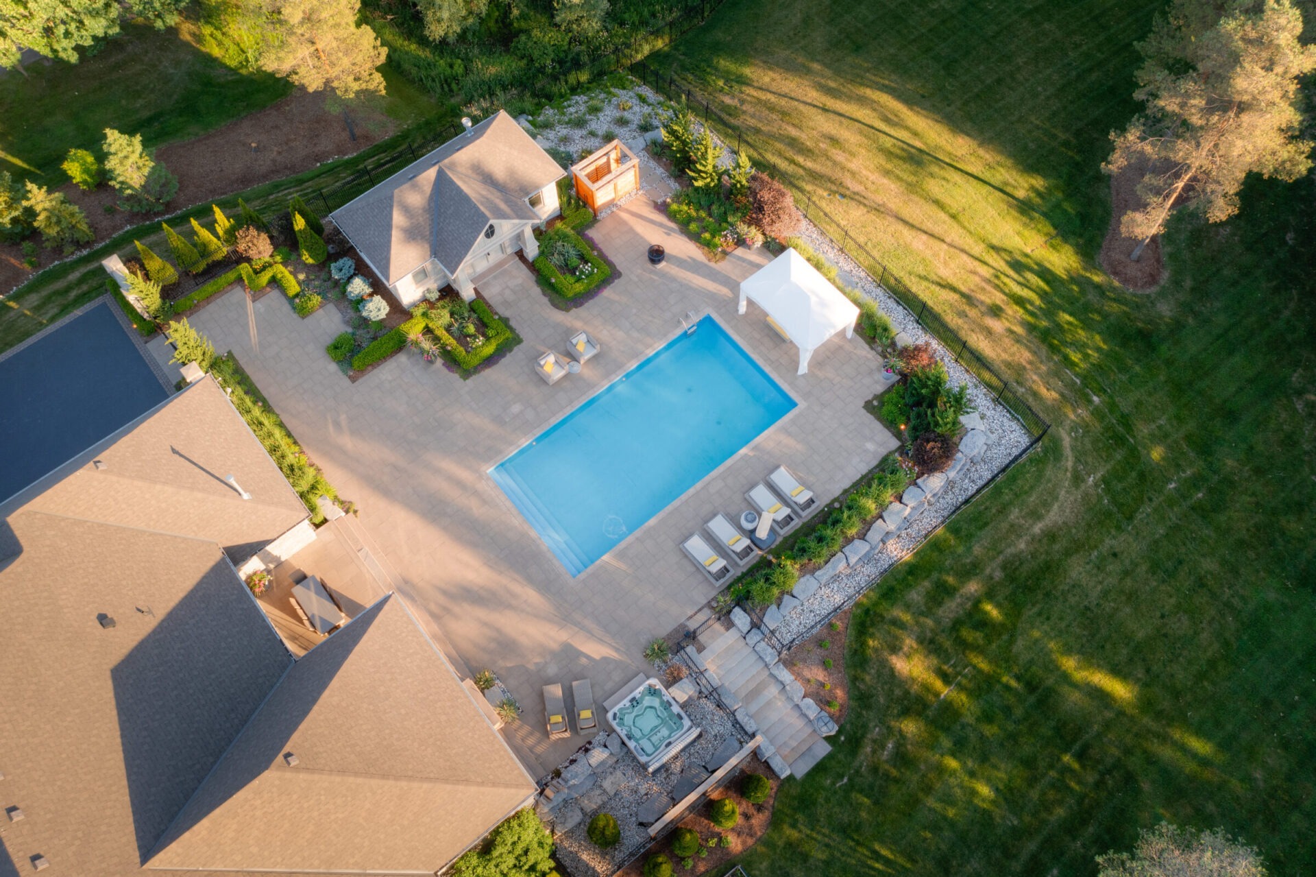 An aerial view of a residential backyard with a large swimming pool, hot tub, landscaped garden, patio area, and a spacious lawn.