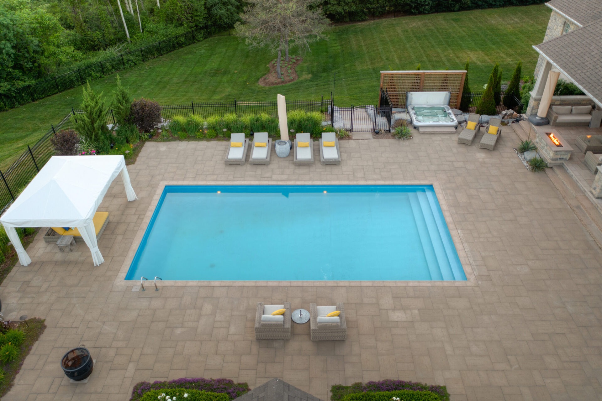 The image shows a residential backyard with a large swimming pool, lounge chairs, a hot tub, a pergola, and a neatly trimmed lawn.