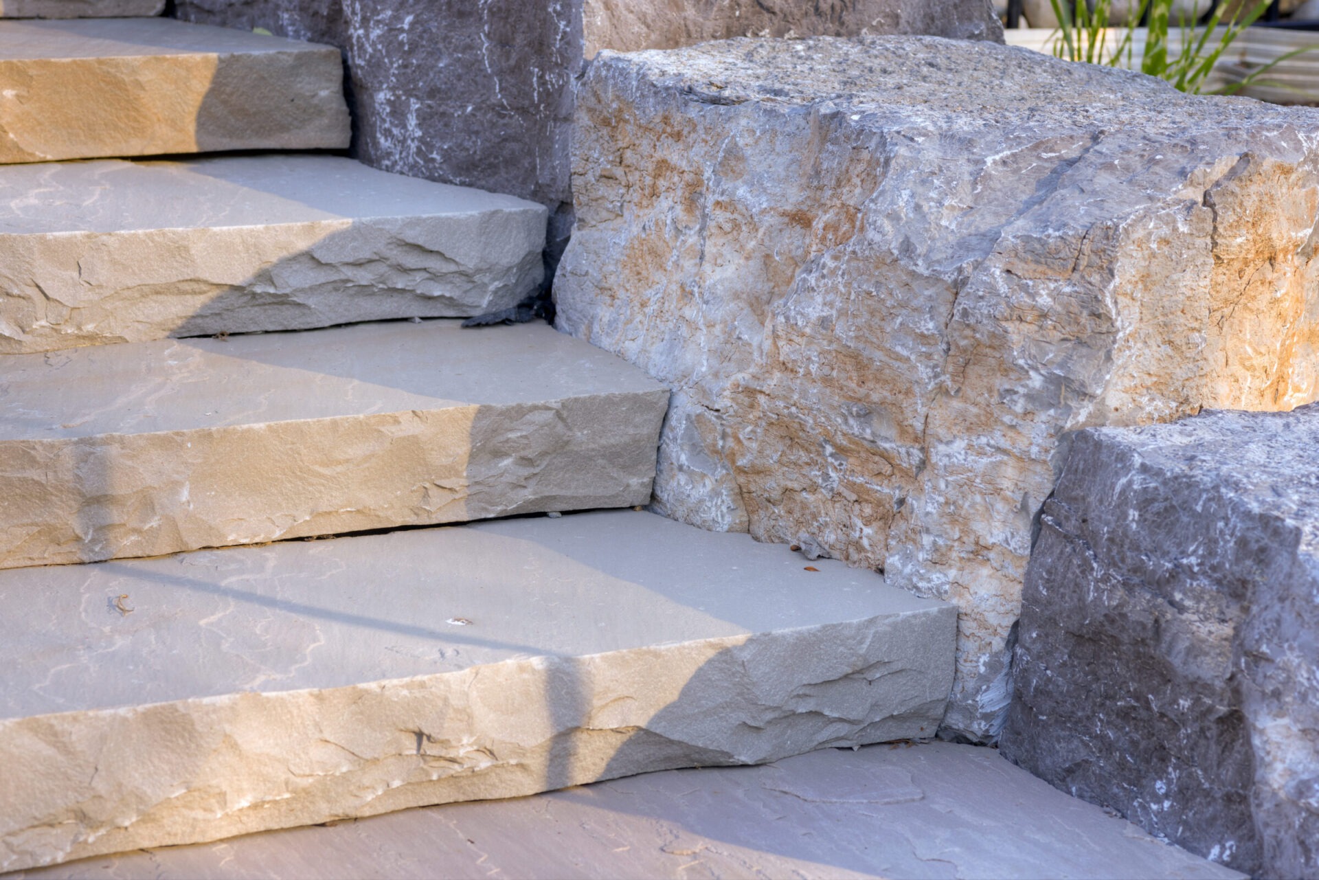 The image shows a set of outdoor stairs made from large textured stone blocks, with sunlight casting shadows on the steps.