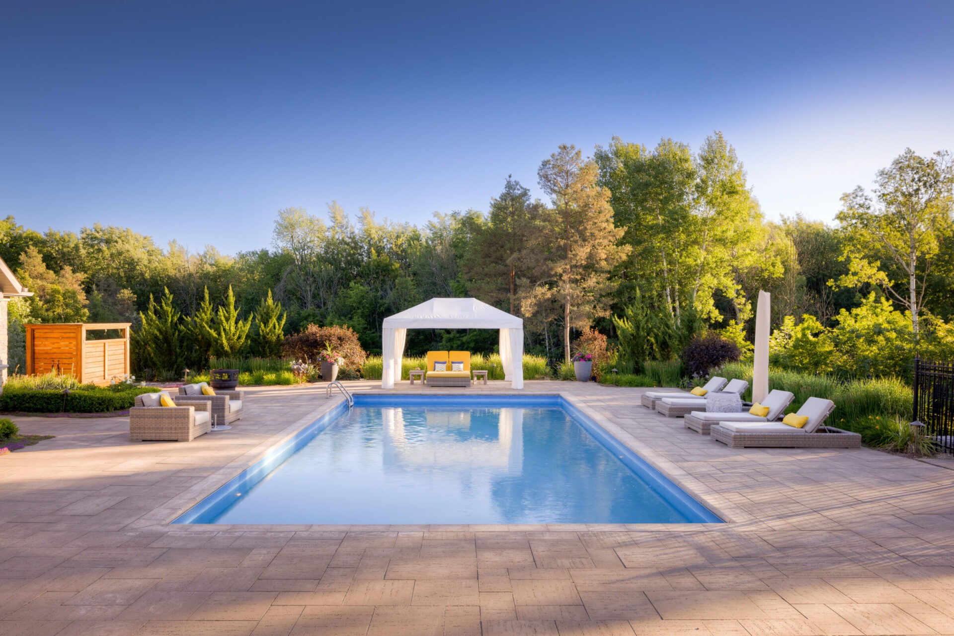 This image features an outdoor swimming pool with clear blue water, flanked by lounge chairs and a gazebo, set against a backdrop of lush greenery.